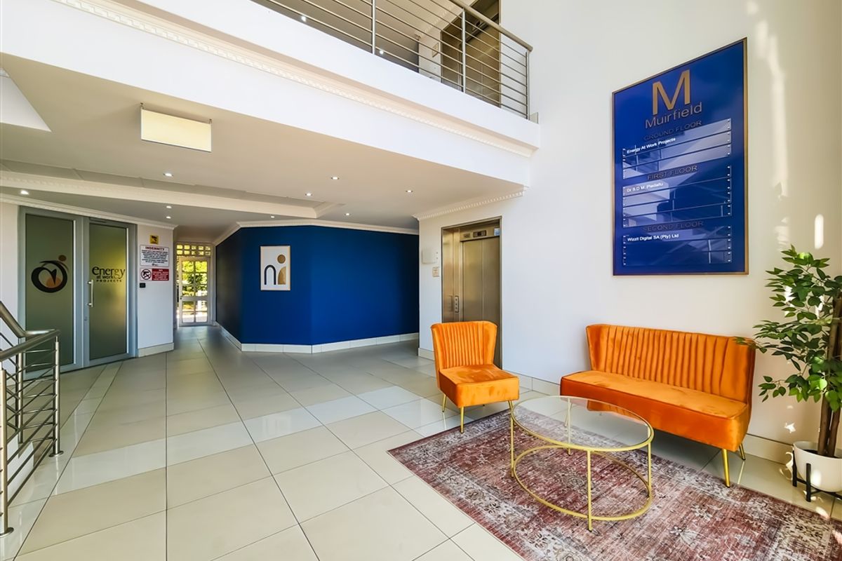 Modern office building lobby featuring a double-volume entrance, stainless steel elevator, mezzanine level, and professional directory signage.