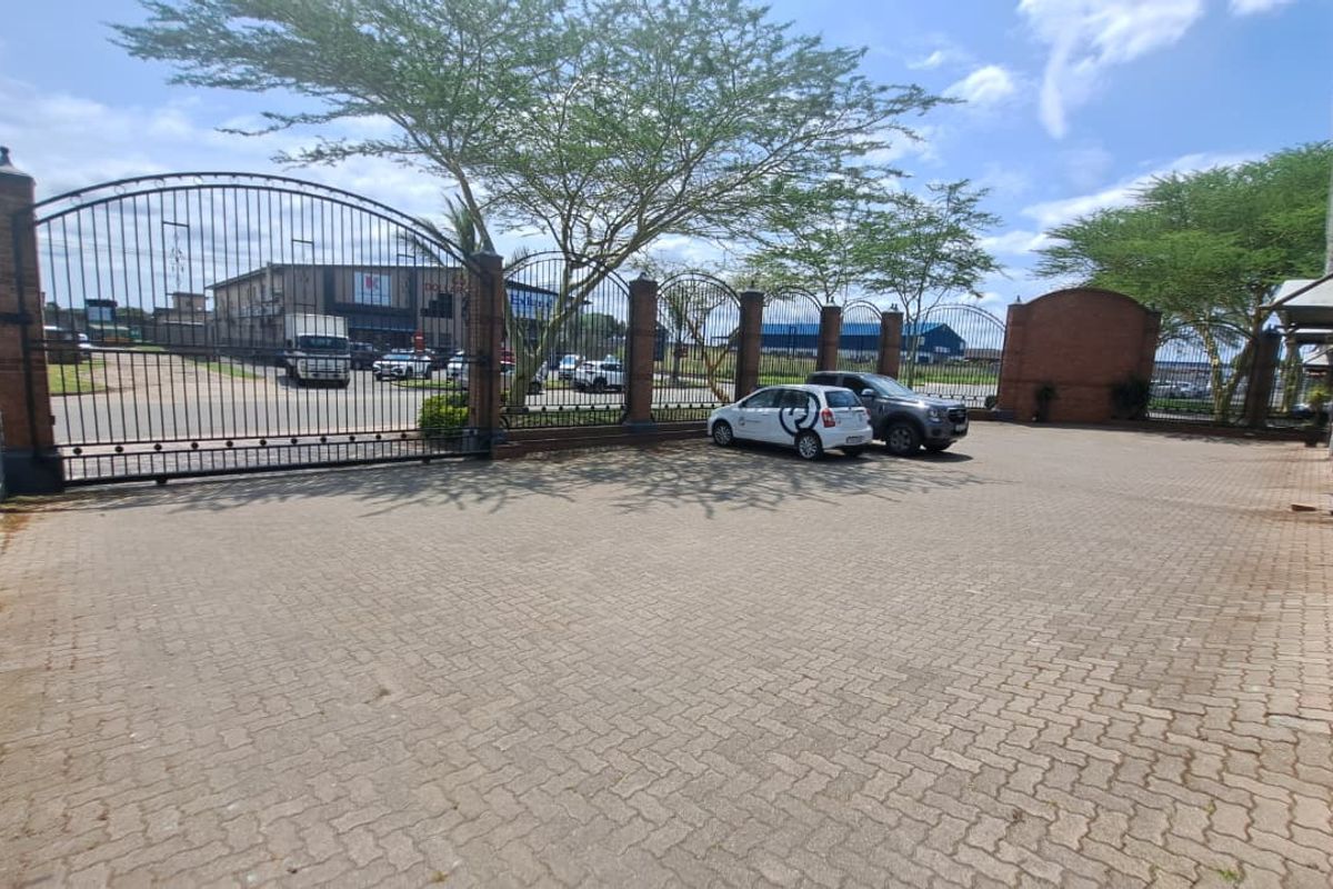 A secure office property entrance featuring a paved driveway, brick perimeter walling, and a large wrought iron security gate.