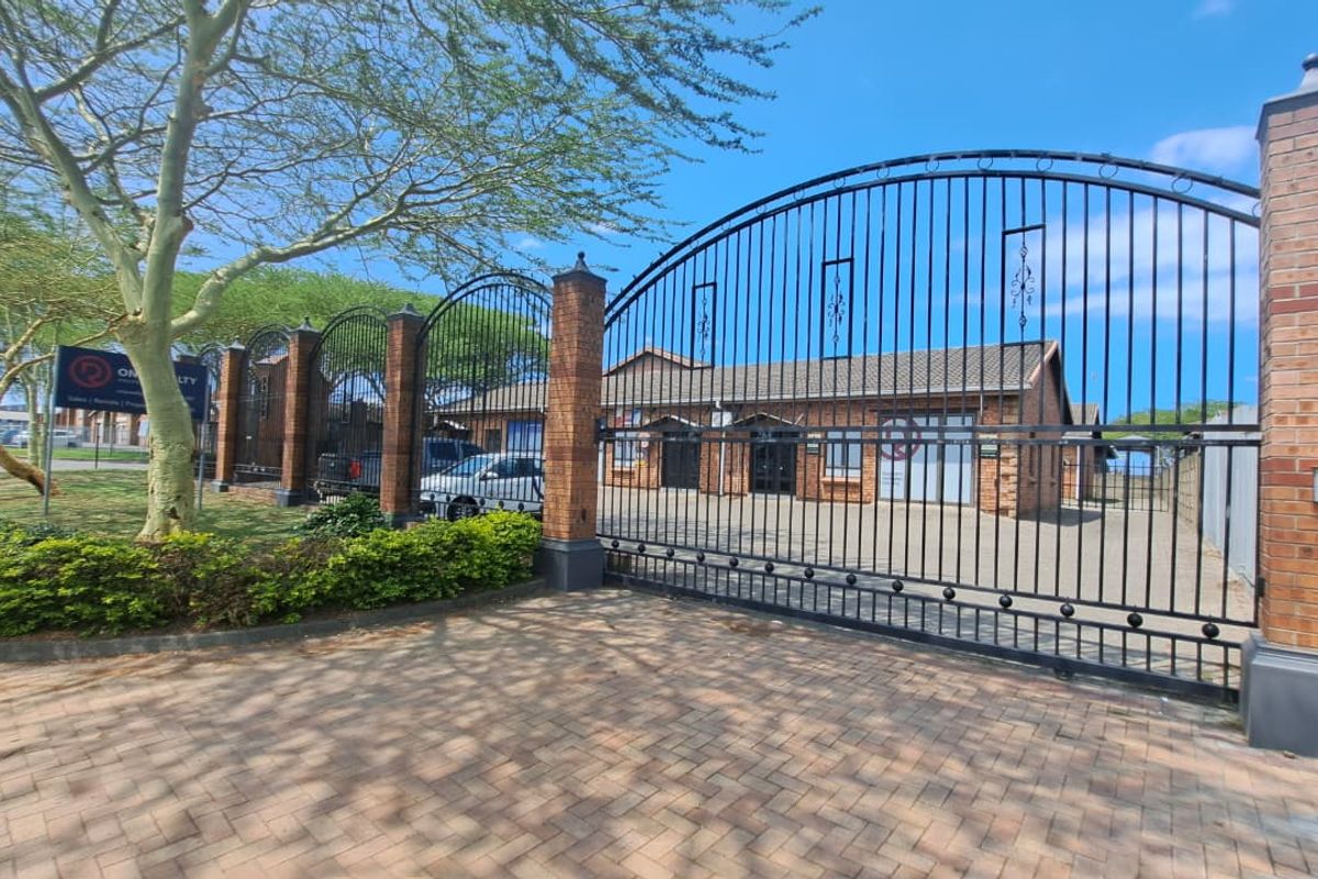 Front view of the office property featuring a secure gated entrance, paved driveway, and brick building facade with a tiled roof.