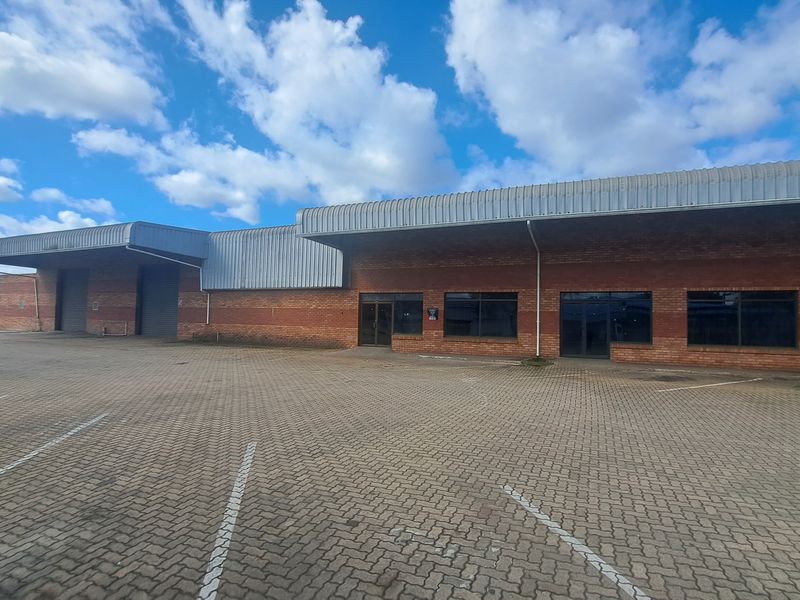 Industrial property featuring a brick facade, metal roofing, multiple roller shutter doors, and an expansive paved parking area for logistics or commercial use.