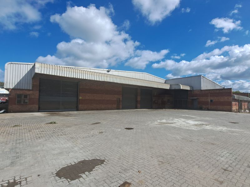 Industrial warehouse facility featuring multiple roller shutter doors, brick exterior construction, and a large paved yard area for vehicle access.