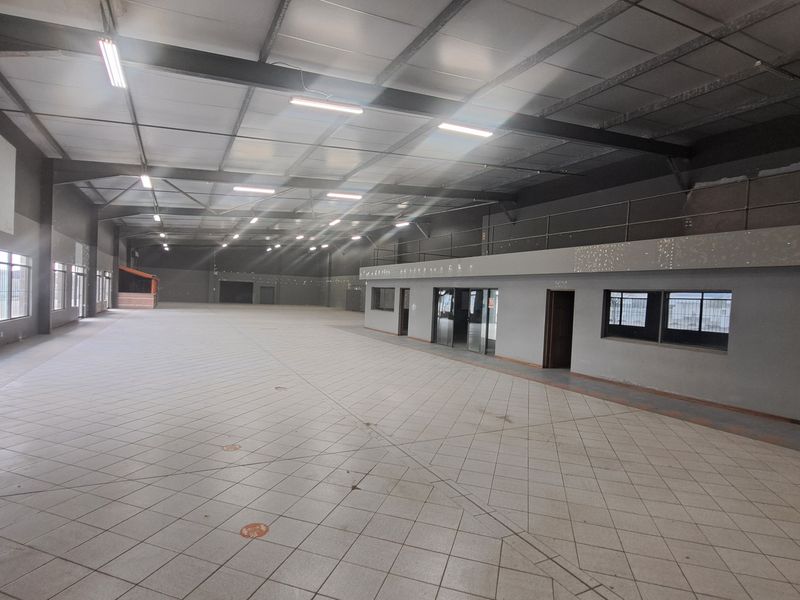 Spacious industrial open-plan warehouse featuring high ceilings with exposed steel trusses, tiled flooring, and a mezzanine level suitable for various commercial or storage uses.