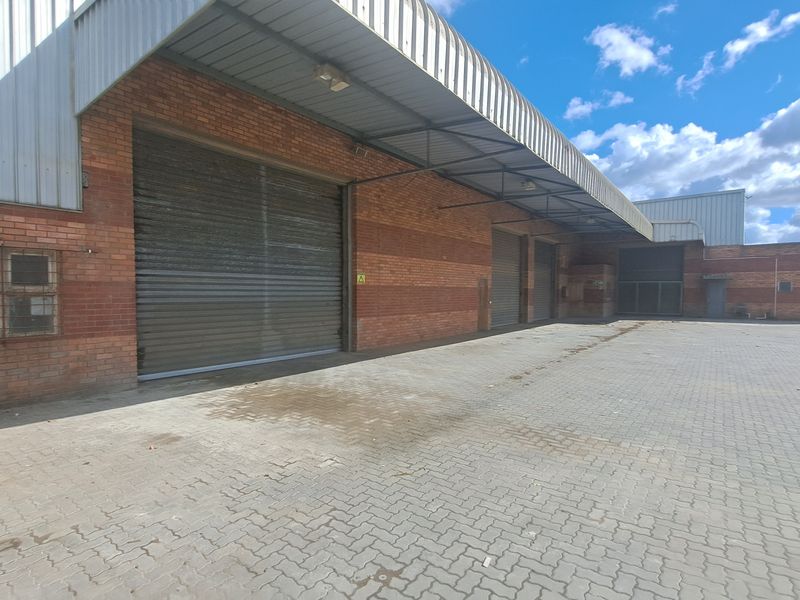 Industrial property exterior featuring multiple roller shutter doors, a protective metal canopy, and a spacious paved yard area.
