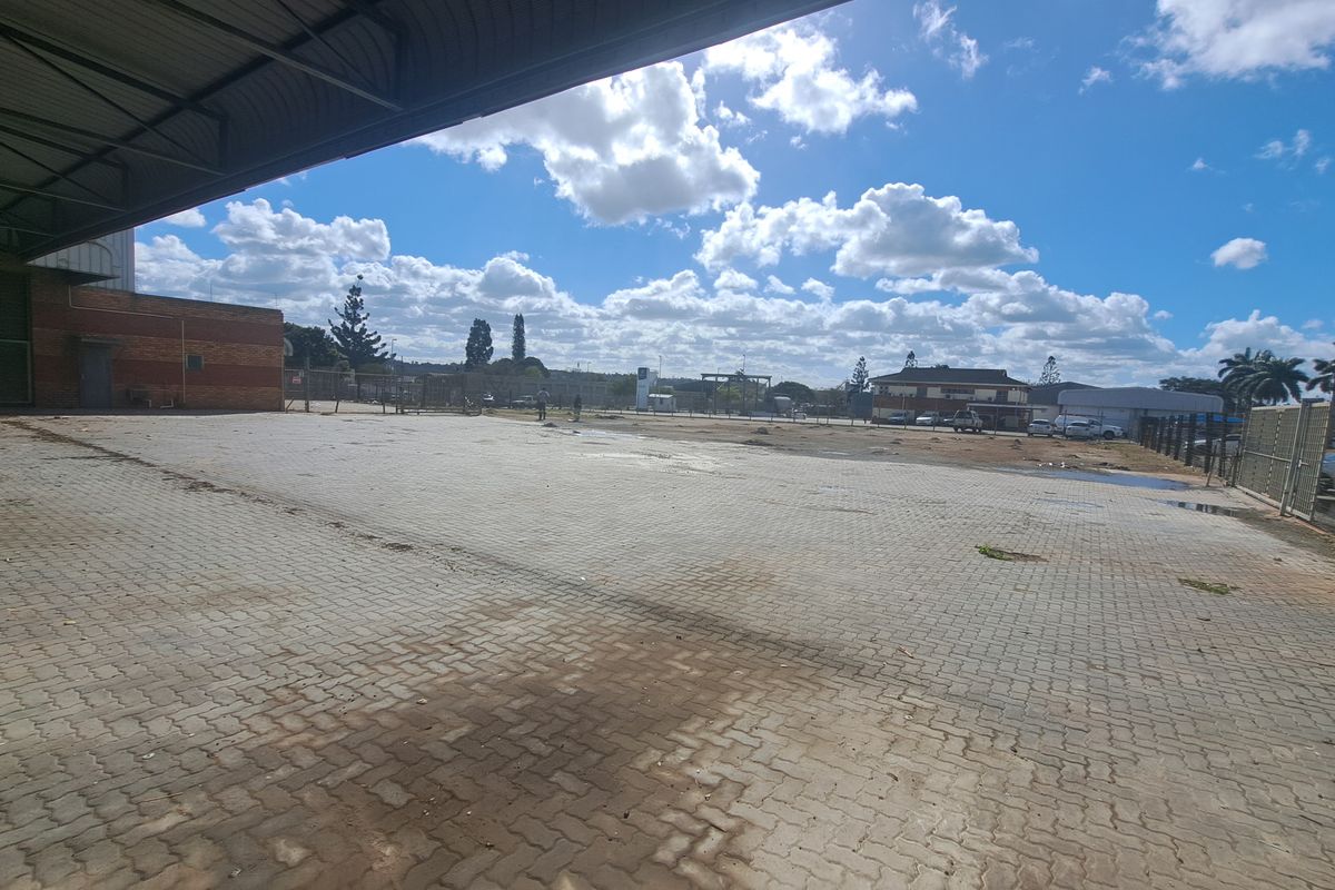 Spacious industrial paved yard with a covered loading bay and perimeter fencing, suitable for logistics or storage operations.