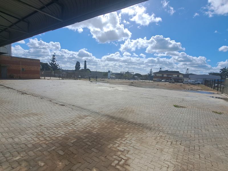 Spacious industrial paved yard with a covered loading bay and perimeter fencing, suitable for logistics or storage operations.