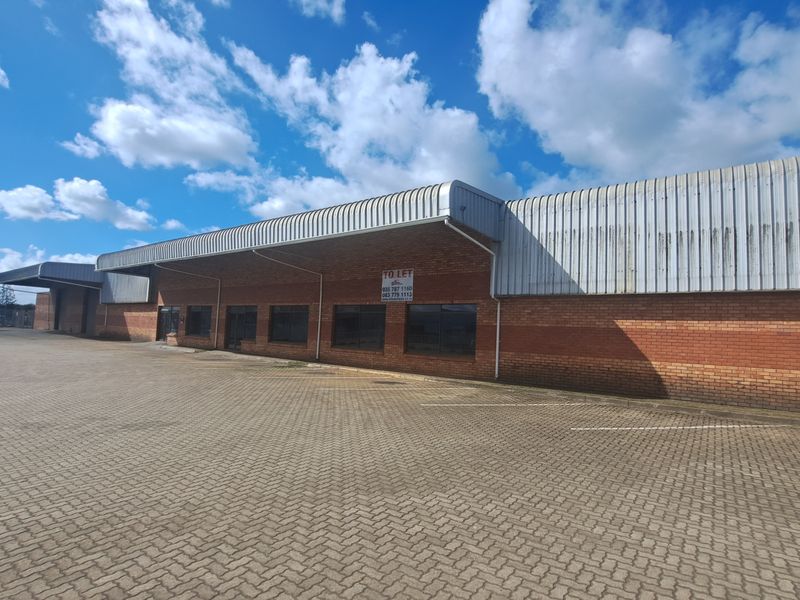 Industrial warehouse exterior featuring a brick facade, metal roofing, and a large paved yard area suitable for logistics or storage.