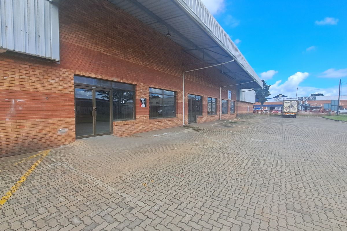 Front elevation of an industrial property featuring a brick facade, metal roof overhang, and paved parking area with aluminium framed glass entry doors.