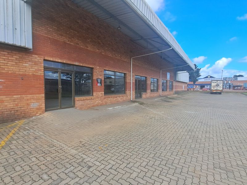 Front elevation of an industrial property featuring a brick facade, metal roof overhang, and paved parking area with aluminium framed glass entry doors.