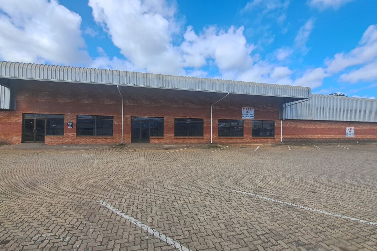 Front elevation of an industrial property featuring a brick facade, metal roofing, and an expansive paved parking area with multiple access points.