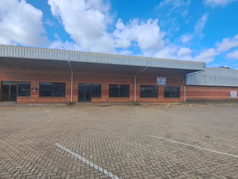 Front elevation of an industrial property featuring a brick facade, metal roofing, and an expansive paved parking area with multiple access points.