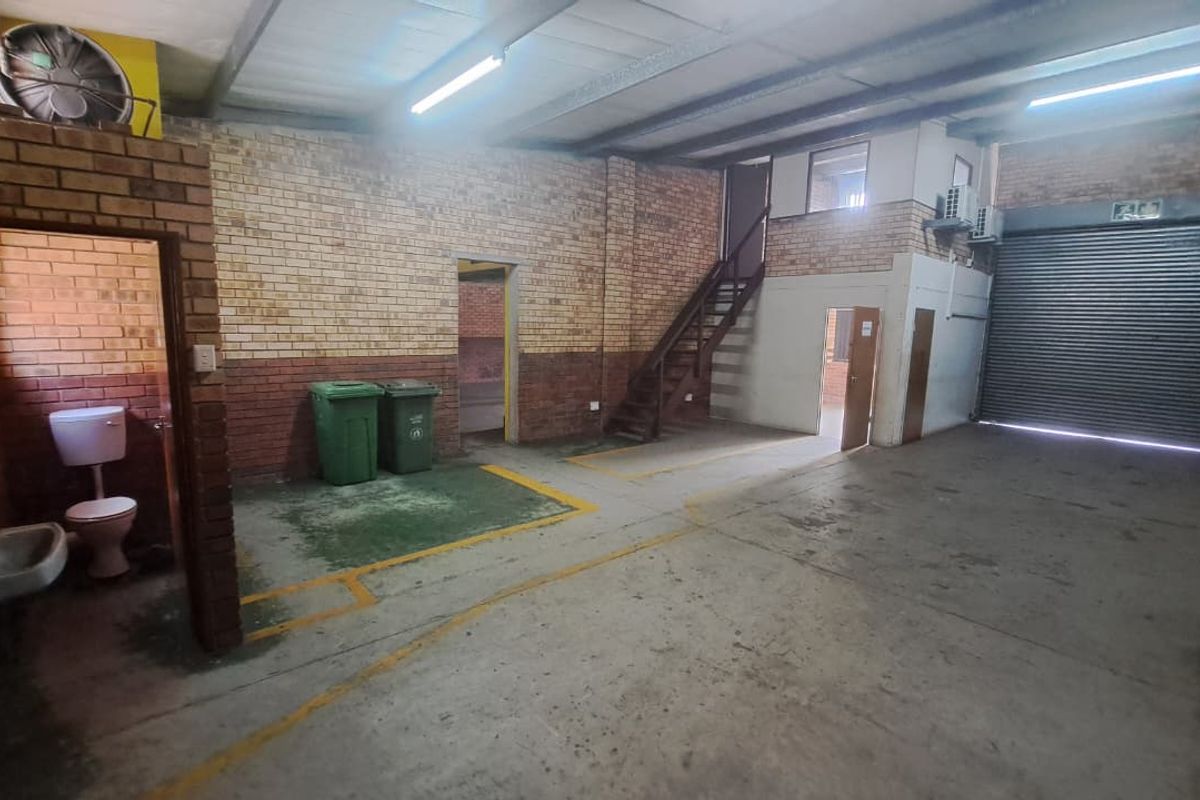 Industrial utility space featuring exposed brick walls, concrete flooring, a roller shutter door, mezzanine access, and an integrated restroom facility.