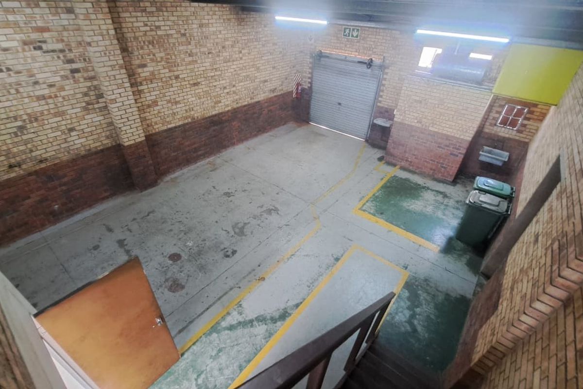 Spacious industrial garage featuring exposed brick walls, concrete flooring with painted markings, and a secure roller shutter door.
