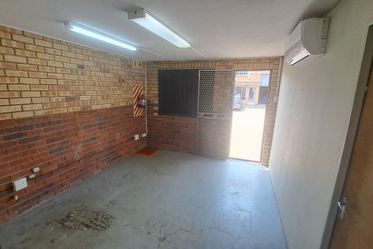 A functional utility space featuring exposed brick walls, concrete flooring, a wall-mounted air conditioning unit, and direct exterior access via a security gate.