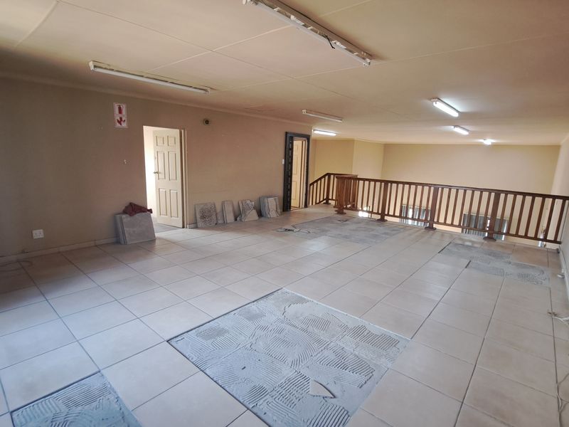 An open-plan office space featuring tiled flooring, a wooden balustrade overlooking the lower level, and wall-mounted air conditioning.