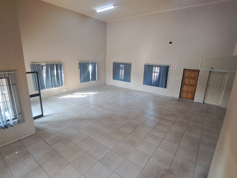 Spacious open-plan industrial unit featuring tiled flooring, high ceilings, vertical blinds, and an internal timber staircase.