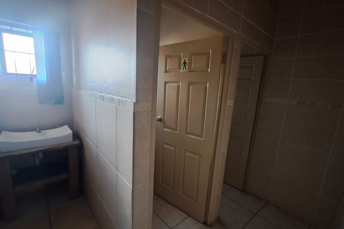 A functional industrial bathroom space featuring tiled walls, a vessel sink on a wooden vanity, and separate access doors.