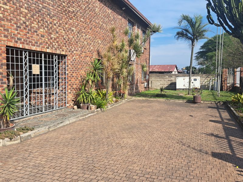 Rear exterior view of an industrial face brick building featuring a paved driveway, security gate, and perimeter wall.