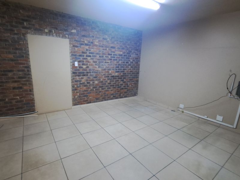 An empty industrial office space featuring an exposed brick wall, ceramic tiled flooring, and functional overhead lighting.