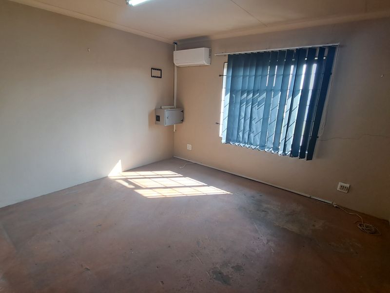 An empty office space featuring an air conditioning unit, electrical distribution board, and vertical blinds, with visible wear to the walls and flooring.