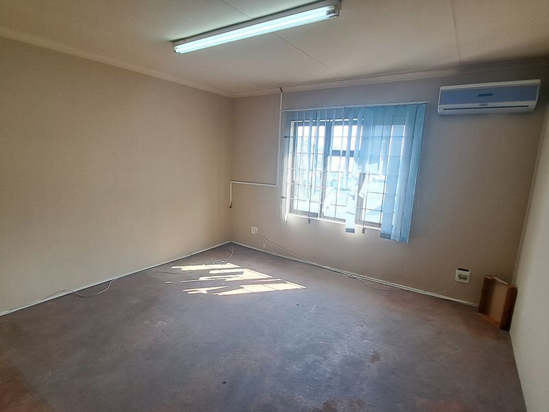An empty office space featuring a split-system air conditioner, fluorescent lighting, and security bars on the window.