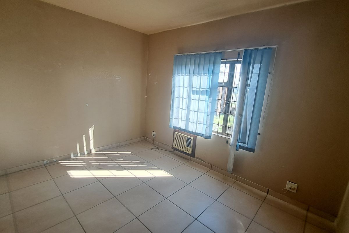 An empty bedroom featuring tiled flooring, a window-mounted air conditioning unit, and vertical blinds, requiring minor cosmetic updates to the walls.