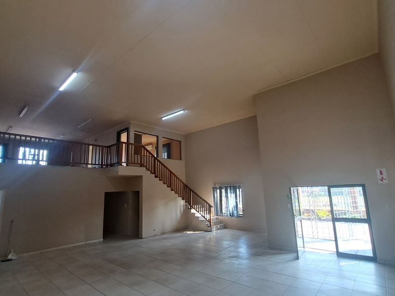 Spacious open-plan industrial unit featuring a mezzanine level, wooden staircase, tiled flooring, and secure access points, suitable for various commercial or office applications.