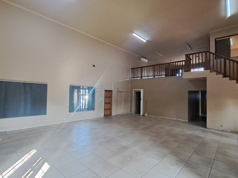 Spacious open-plan industrial area featuring tiled flooring, a mezzanine level with a wooden staircase, and ample natural light through multiple windows.