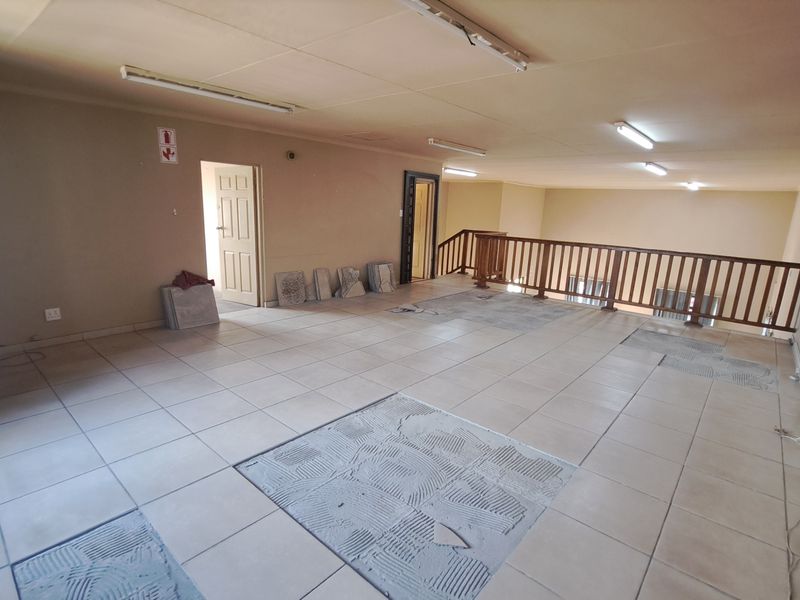 An open-plan industrial mezzanine level featuring tiled flooring, a wooden balustrade, and air conditioning, currently undergoing floor maintenance with missing tiles.