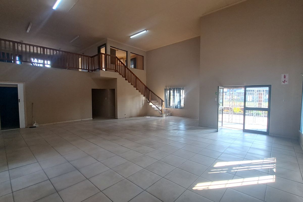 Spacious open-plan industrial unit featuring a mezzanine level, wooden staircase, tiled flooring, and ample natural light through large windows and a security entrance.