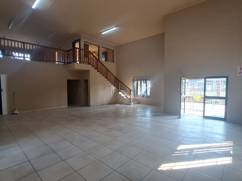 Spacious open-plan industrial unit featuring a mezzanine level, wooden staircase, tiled flooring, and ample natural light through large windows and a security entrance.