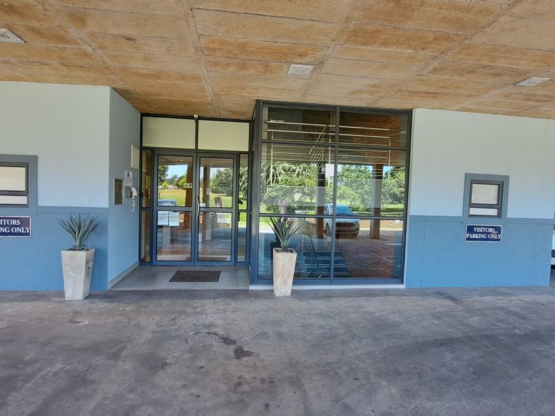 Main office building entrance featuring a covered driveway, glass door entry, and aluminium window frames with designated visitor parking signage.