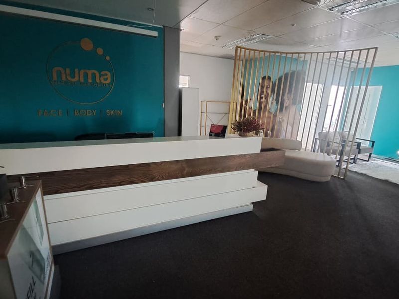 A professional office reception area featuring a modern built-in desk, teal accent wall, and open-plan layout with suspended ceiling tiles.