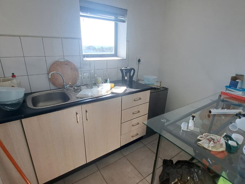 A functional scullery area featuring a stainless steel sink, tiled splashback, and laminate cabinetry, providing practical utility space for office operations.