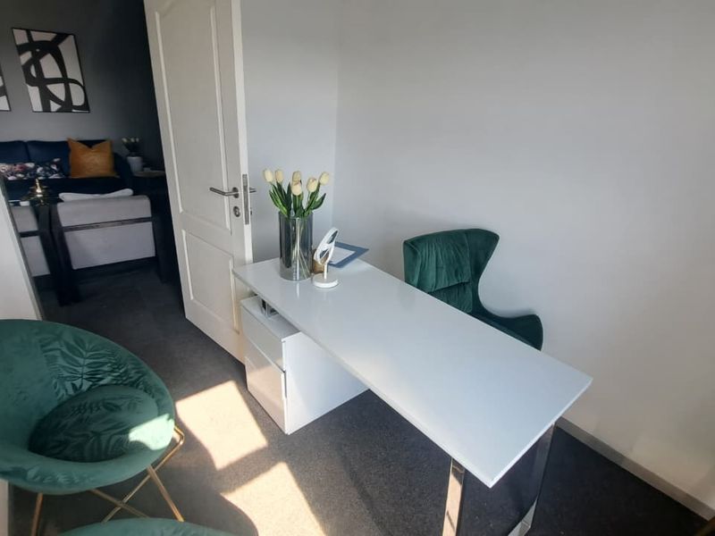 A compact office space featuring neutral wall finishes, carpeted flooring, and an internal door leading to an adjacent room.