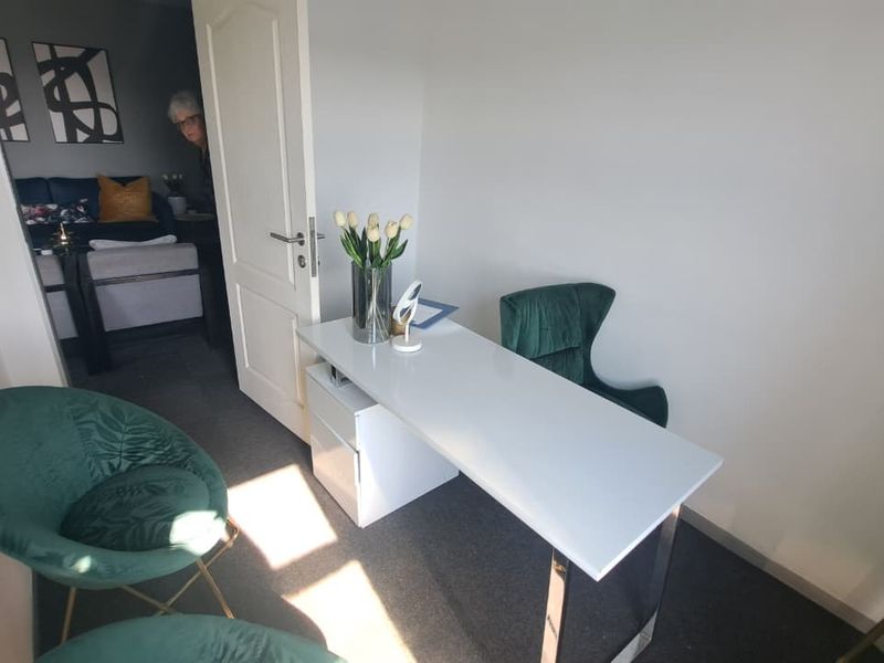 A compact office space featuring neutral wall finishes and carpeted flooring, with an adjoining room visible through the doorway.