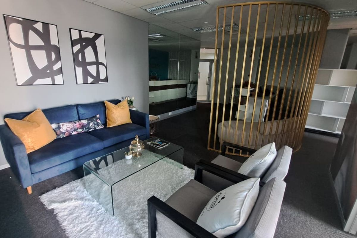 A modern office reception or waiting area featuring a mirrored wall, suspended ceiling, and a decorative gold-toned metal privacy screen.