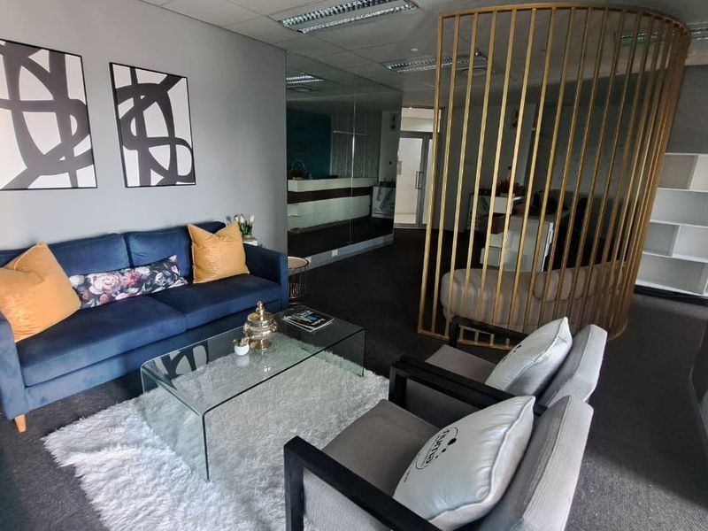 A modern office reception or waiting area featuring a mirrored wall, suspended ceiling, and a decorative gold-toned metal privacy screen.
