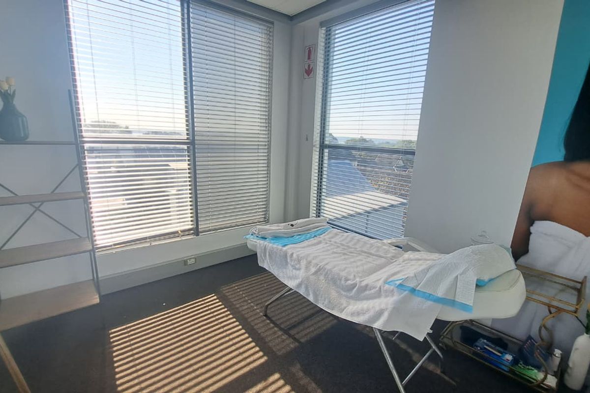 A bright office or treatment room featuring large windows with venetian blinds and carpeted flooring, suitable for professional use.