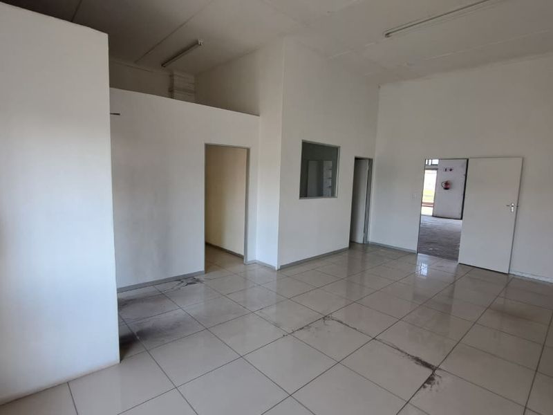 An empty industrial office space featuring tiled flooring, fluorescent lighting, and multiple access points, suitable for a variety of commercial or administrative uses.