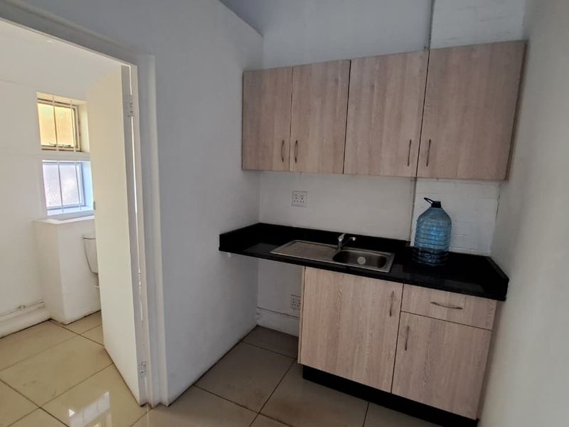 A functional scullery area featuring built-in cabinetry, a dark laminate countertop with an integrated stainless steel sink, and tiled flooring.