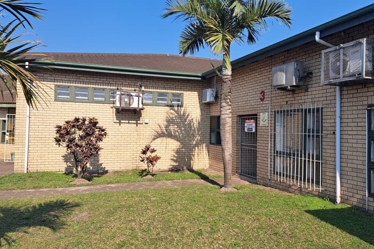 Exterior view of an industrial property featuring face brick construction, security bars on windows, and external air conditioning units with a paved walkway.
