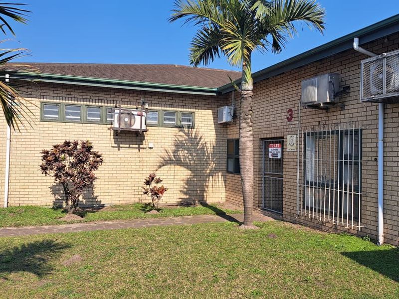 Exterior view of an industrial property featuring face brick construction, security bars on windows, and external air conditioning units with a paved walkway.