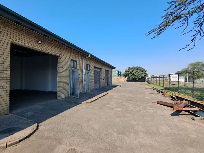Exterior view of an industrial property featuring face brick facade, multiple roller shutter doors, security gates, and a concrete apron with perimeter fencing.