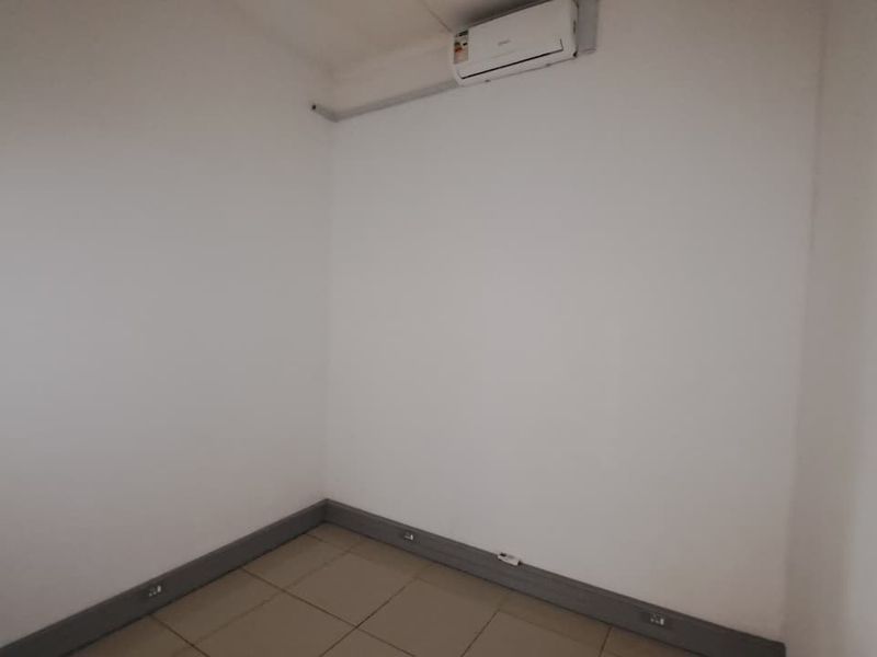 A clean, empty office space featuring tiled flooring, neutral walls, and a wall-mounted split-system air conditioning unit.