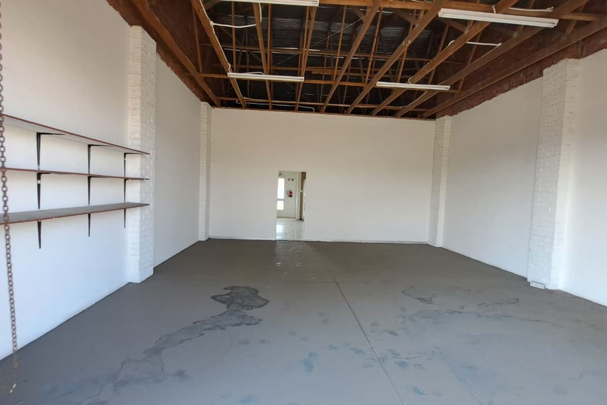 An open-plan industrial utility space featuring exposed timber roof trusses, painted brick columns, and concrete flooring with wall-mounted shelving.
