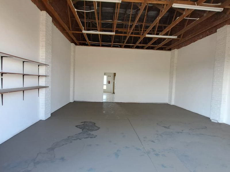 An open-plan industrial utility space featuring exposed timber roof trusses, painted brick columns, and concrete flooring with wall-mounted shelving.