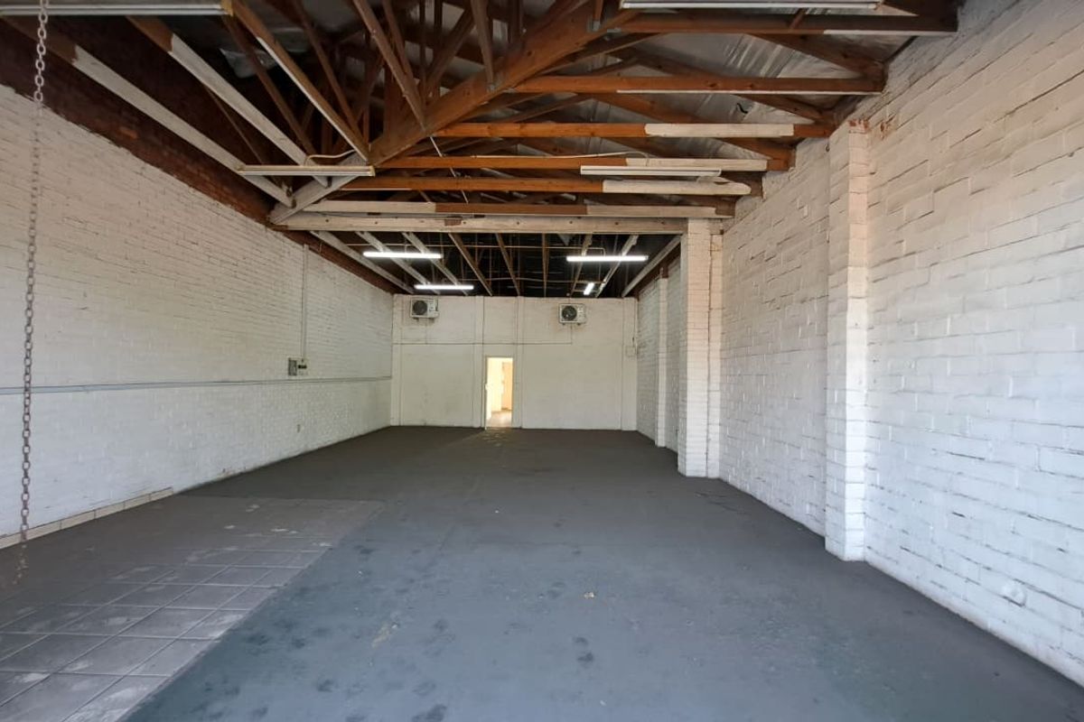 Spacious industrial utility area featuring exposed timber roof trusses, painted brick walls, and wall-mounted air conditioning units, suitable for various commercial or storage uses.