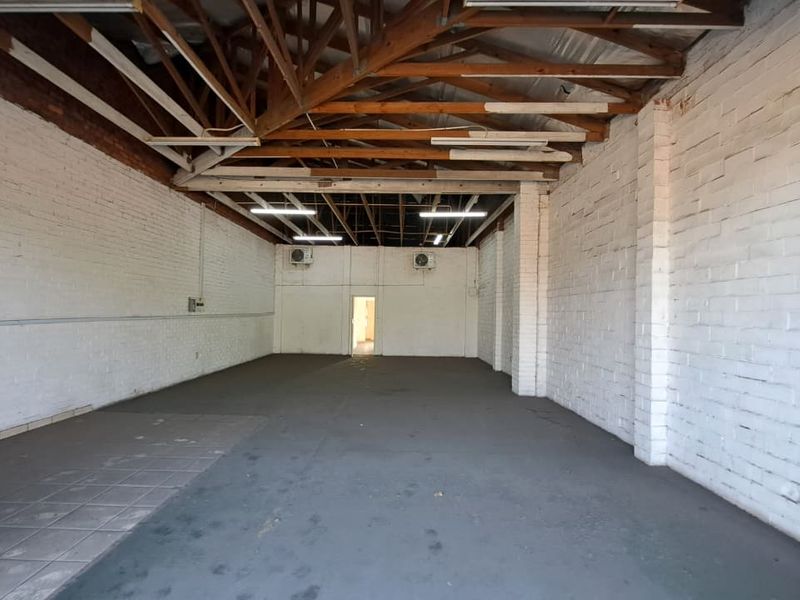 Spacious industrial utility area featuring exposed timber roof trusses, painted brick walls, and wall-mounted air conditioning units, suitable for various commercial or storage uses.