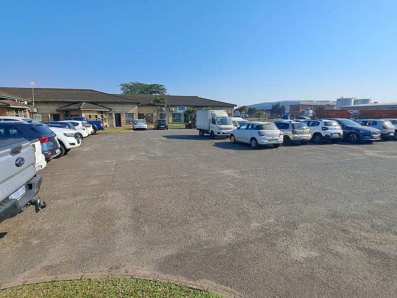 Wide-angle view of an industrial property featuring a large asphalt parking area and building frontage with tiled roofing.