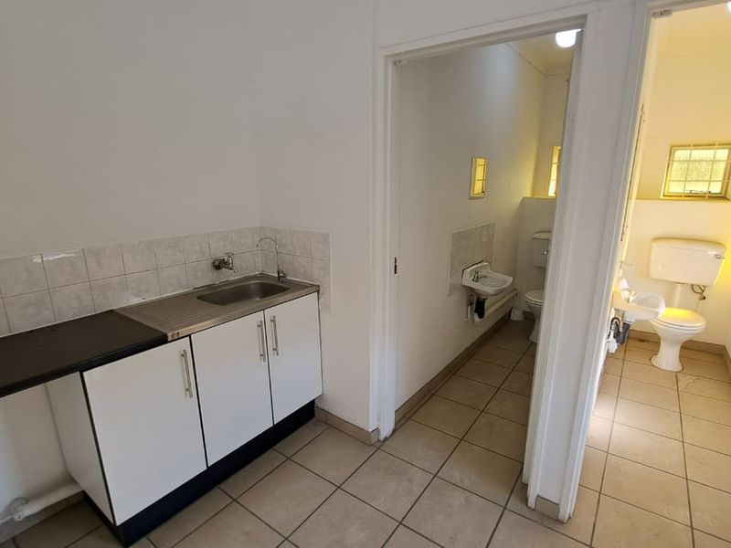 A functional utility area featuring a built-in sink with cabinetry, tiled flooring, and access to two separate toilet facilities.